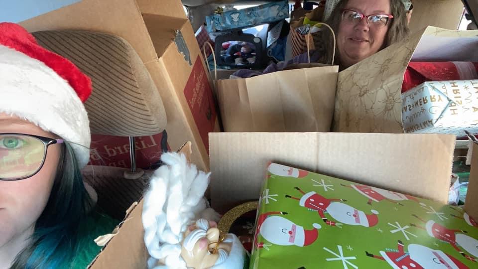 Two Volunteers in a car so filled with gift donations you can barely see them peeking out