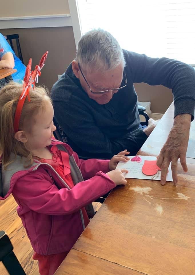 Elderly man opening up a handmade valentine with a little girl
