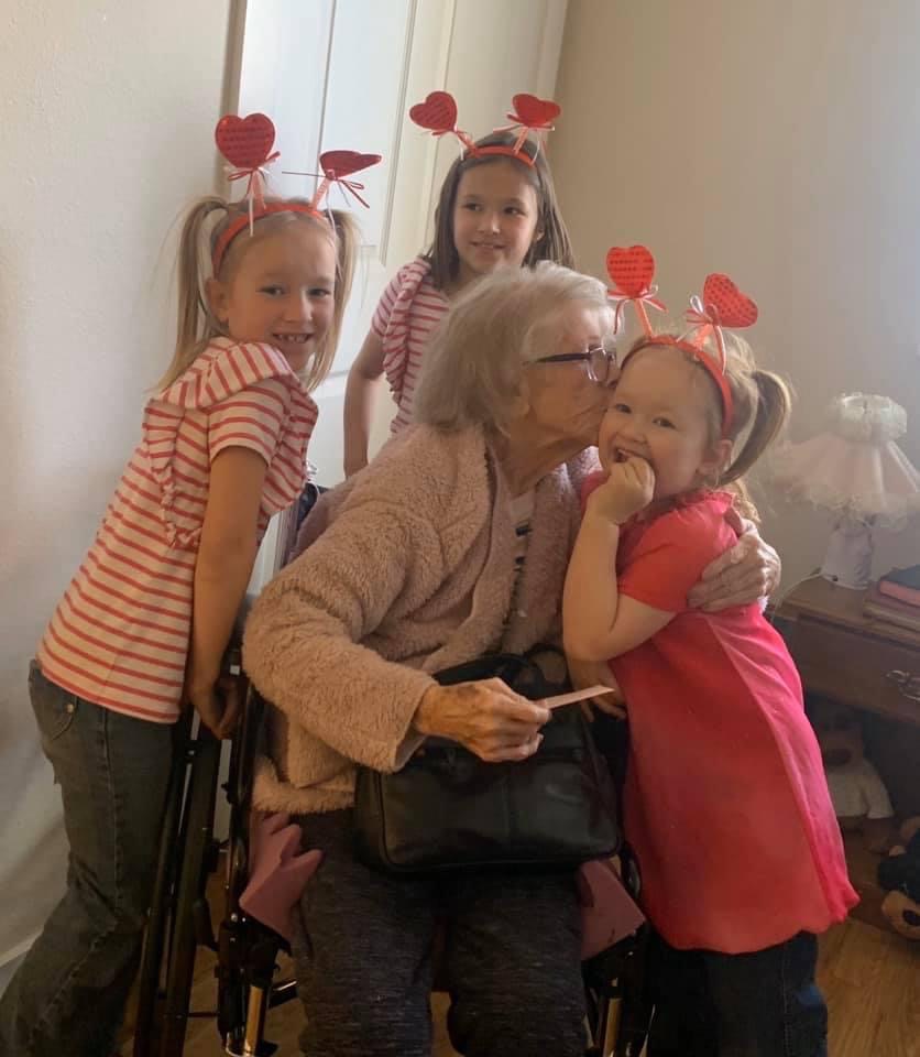 Three little girls with an elderly woman in a wheelchair - one of the girls is getting a kiss.
