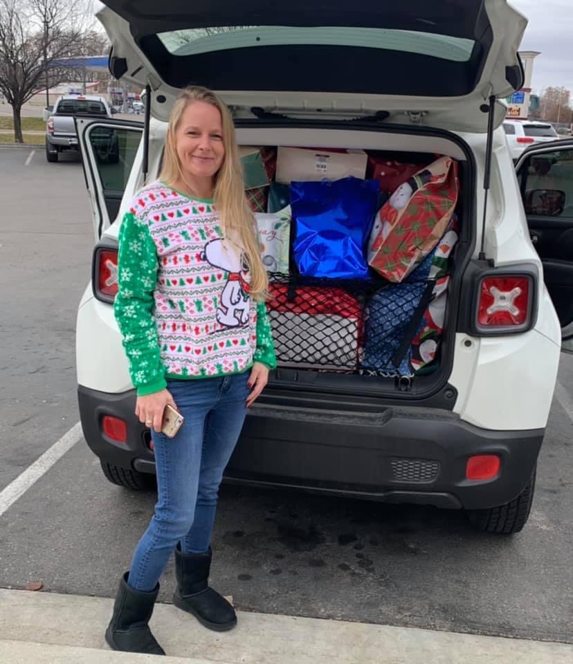 Volunteer in front of a vehicle and the trunk is completely filled with wrapped gifts