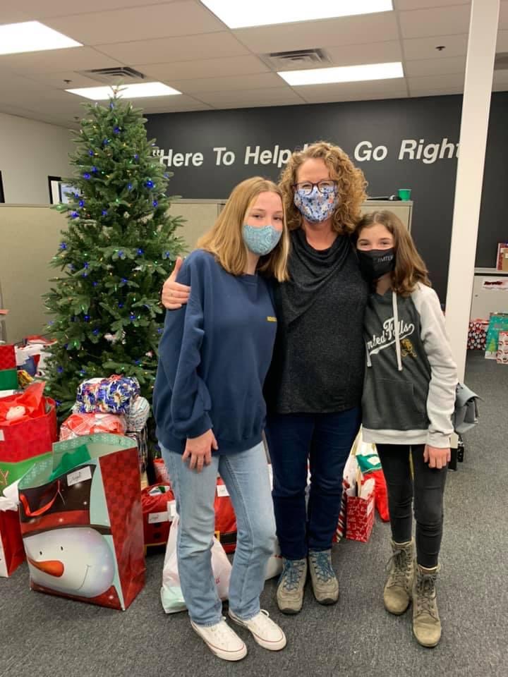 Three people standing in front of a tree surrounded by donations they have wrapped