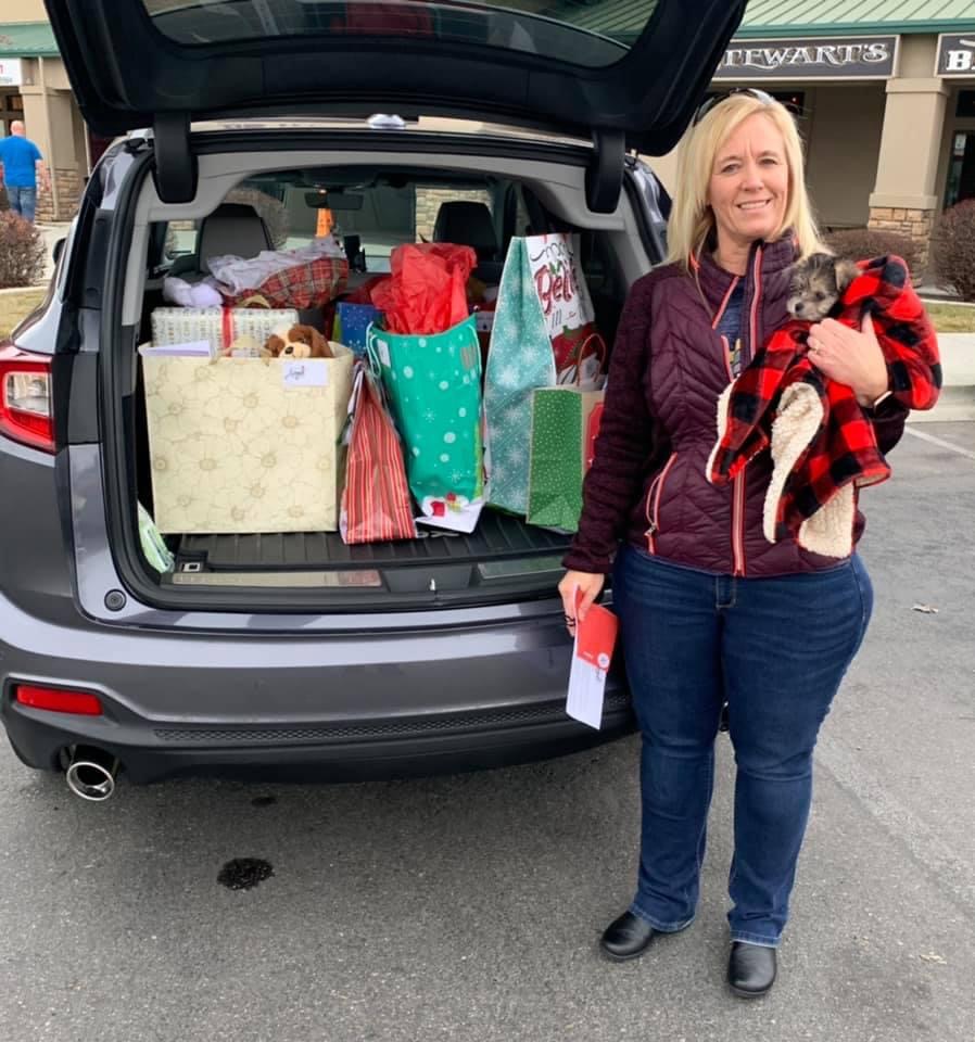 A female volunteer and her little dog dropping off a trunk full of gift bag donations