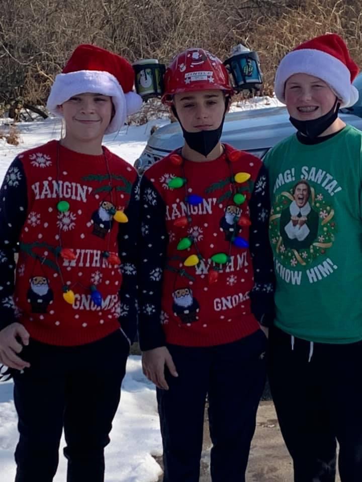 Three teen boy volunteers in masks posing with their ugly sweaters